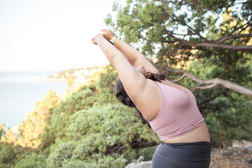 Beautiful woman makes healthy yoga exercises for fot body outdoor in the nature. Young woman dresse sport wear for overweight people.