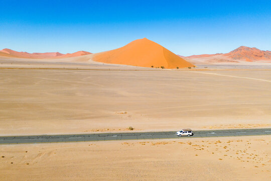 Drone image of offroad vehicle driving on desert road in Sossusvlei, Namibia with high orange sand dunes © Thomas