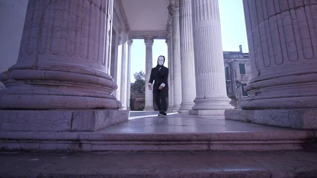 Masked person dances among the columns of the building