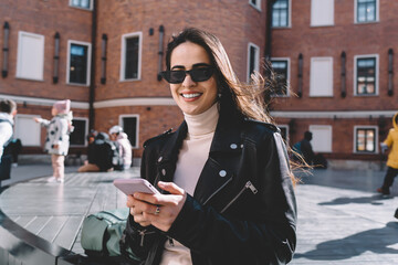 Positive woman smiling and chatting on smartphone on street