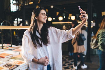 Cheerful woman taking selfie near books table