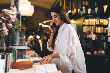 Cheerful woman talking on mobile phone in bookstore
