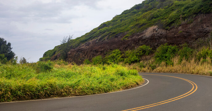 Close-up of a curve in the road and cloudy sky through the green hills along a scenic drive in West Maui; Maui, Hawaii, United States of America