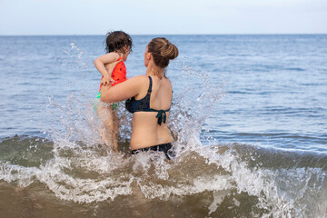 View taken from behind of a mother and daughter playing in the waves of the Pacific Ocean at Kamaole Beach; Maui, Hawaii, United States of America