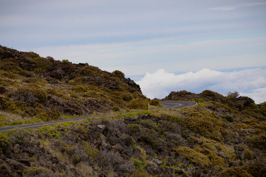 Scenic view of a sharp turn on mountain highway with view of the clouds over the mountainside on the Road down from Haleakala; Maui, Hawaii, United States of America