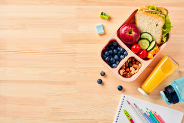Back to school concept. Lunch box with healthy meal, paper notebook, colorful school stationery on wooden desk table