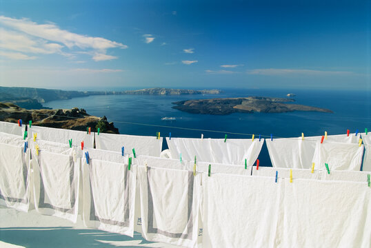 Crisp white linens hanging out to dry with a scenic hilltop view of the water; Santorini, Greece