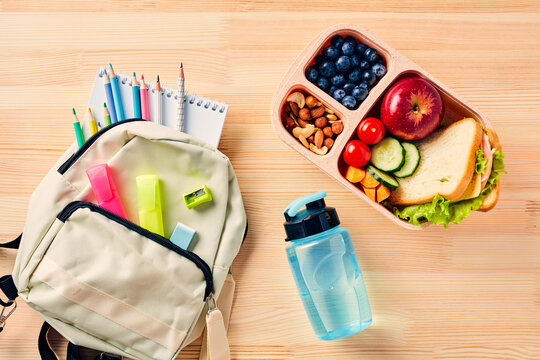 Back to school concept. Healthy lunch box and backpack of colorful school supplies on wooden table, top view, flat lay.