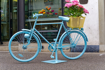 Fototapeta na wymiar Blue painted bicycle with basked with pink hydrangea flowers at the old town of Swiss City of Winterthur on a cloudy spring day. Photo taken May 17th, 2023, Winterthur, Switzerland.