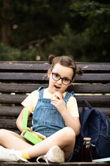 Cute little schoolgirl eating from lunch box outdoor sitting on a bench. Food for kids.