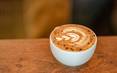 Hot coffee cup with latte art milk foam on wood background.