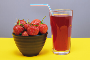 Fresh strawberry and juice. Black bowl with strawberries and glass of red juice on yellow and gray background.