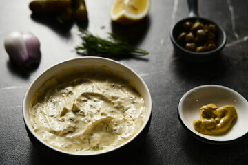 Classic Tartar Sauce with it ingredients on dark stone or marble background. Mayonnaise with dill and pickled cucumbers with lemon. 