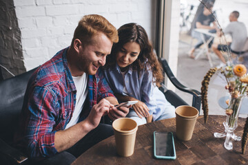 Cheerful couple using smartphone in cafe