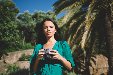 Happy ethnic woman standing with photo camera in hands