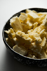 Broken white chocolate in a black ceramic bowl. The main ingredient for making blondies. White marble background. Close up.