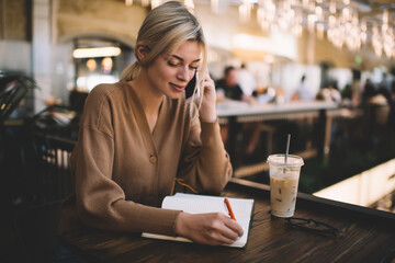 Caucasian woman with education textbook making consultancy conversation for discussing plan notes, millennial female student with notepad using smartphone technology for calling via application