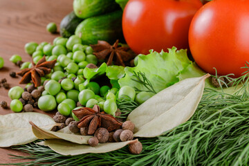 A set of several cucumbers, pea, dill, lettuce, tomato branch, bay leaf, pepper, anise, lie on the wooden table. Fresh raw organic vegetables closeup.