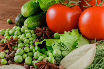 A set of several cucumbers, pea, dill, lettuce, tomato branch, bay leaf, pepper, anise, lie on the wooden table. Fresh raw organic vegetables closeup.