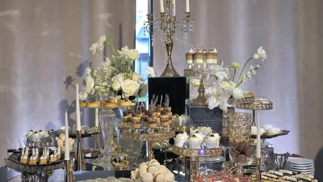 Stylish luxury candy bar in gold colours. Sweet cakes and candies with muffins. People have fun and rest on the event. Beautiful festive decoration. Decor on the evening party.