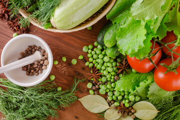 Fresh raw organic vegetables. A set of several cucumbers, dill, lettuce, tomato, zucchini, pepper, anise, bay leaf, spices, green peas lie on the wooden table. Closeup. Top view.