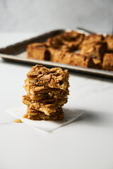 Stack of squares of Blondie cookies with pecan nuts on white marble countertop. White chocolate sweet and tasty, chewy cookie bars. 