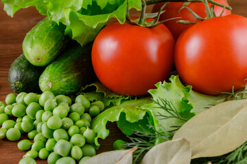 A set of several cucumbers, pea, dill, lettuce, tomato branch, bay leaf lie on the wooden table. Fresh raw organic vegetables closeup.