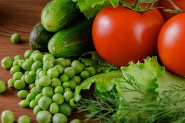 A set of several cucumbers, pea, dill, lettuce, tomato branch lie on the wooden table. Fresh raw organic vegetables closeup.