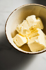 Unsalted butter cubes in white bowl on white marble background. The oil is at room temperature, soft and fluffy. 