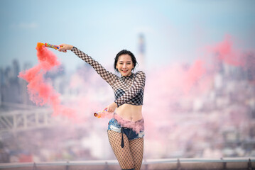 Fototapeta na wymiar Beautiful Asian female hip hop dancer striking a sexy dance pose, attractive sexy dancer women dancing with colored smoke bomb on rooftop with skyscraper city view, hip hop street dance
