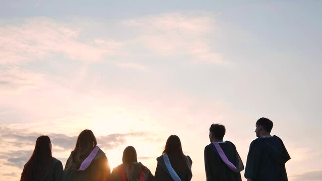 Silhouettes of graduates toss their caps at sunset.