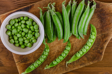 Fresh green pea and pea pods. Pea in bowl and pea pods on wooden board. Top view.