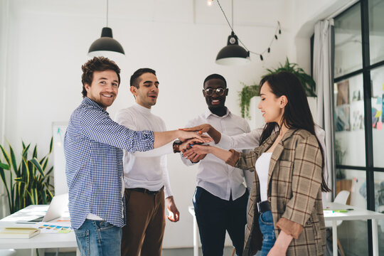 Cheerful multiethnic colleagues stacking hands together in creative workspace