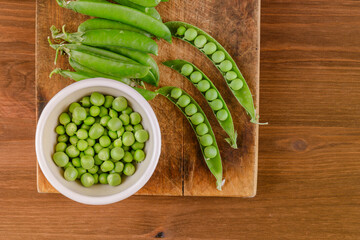 Fresh green pea and pea pods. Pea in bowl and pea pods on wooden board. Top view.