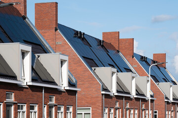 Solar panels mounted on the roofs of a row modern new-build social rental houses in Lemmer, Friesland, the Netherlands with blue sky