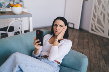 Worried young female with mobile phone reading news on internet