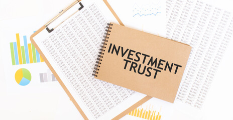 Text INVESTMENT TRUST on brown paper notepad on the table with diagram. Business concept