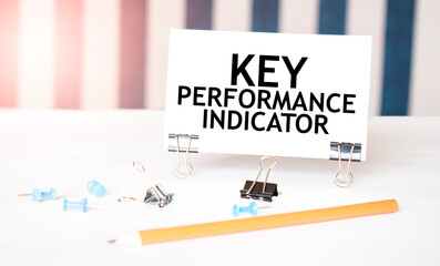 KEY PERFORMANCE INDICATOR sign on paper on white desk with office tools. Blue and white background
