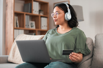 Woman, laptop and credit card with headphones and online shopping on sofa, music subscription...