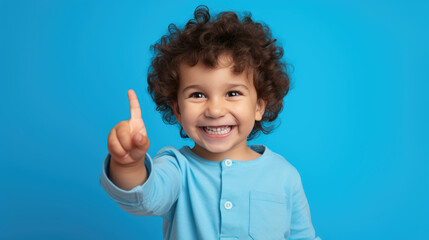 Child wearing casual clothes pointing with hand and finger to the side looking at the camera.