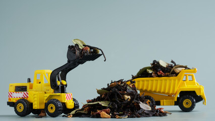 A pile of dry black tea flavored with fruits and flower petals next to a toy forklift and dump truck. Tea harvesting and transportation. Toy world. Photo. Selective focus.