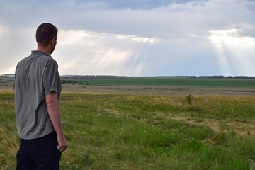A man stands in a field and looks at the sunset descending rays of the sun