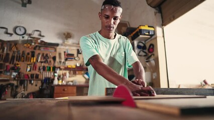 Young carpenter using saw machine to slice wood at workshop. Focused apprentice at carpentry artisan craftmanship store