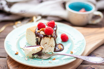 Slice of vanilla cheesecake with chocolate sauce, fresh raspberry and nuts on blue plate, close up view