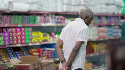 Back of a senior customer browsing at products at grocery store, looking at items to buy on shelf. Elderly shopper in candid scene, consumer lifestyle