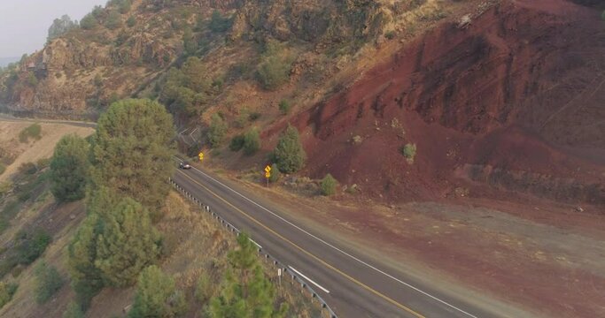 flying over a car driving on a mountain road past a road cut with red soil