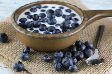 Blueberries in a bowl with milk on a wooden table with burlap. 