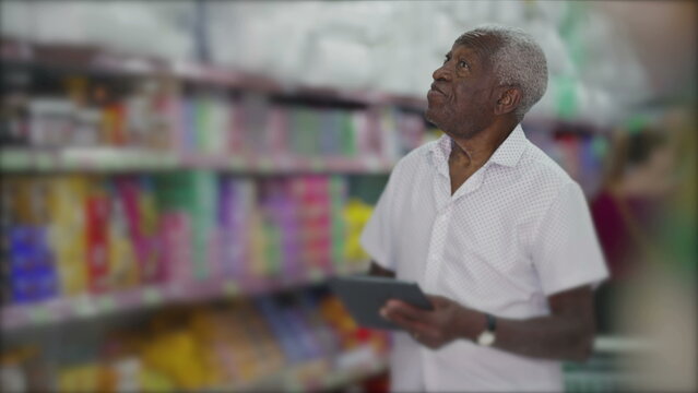 One black manager of grocery store browsing inventory with tablet device standing in aisle. Small business owner inspecting products with modern technology