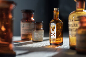 Poison bottle with skull and bones stands among pharmaceutical bottles. Danger sign, symbol of death. Concept background on poison poisoning, pharmaceutical, chemistry, medical, old science topic. - 627473126