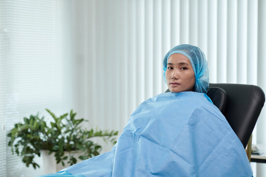Young woman with marks on face sitting in chair in office of plastic surgeon